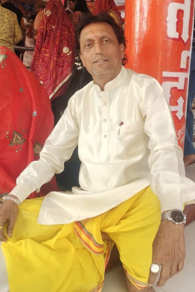 Pandit Ashok Thakur (Guruji) smiling, dressed in traditional orange attire.